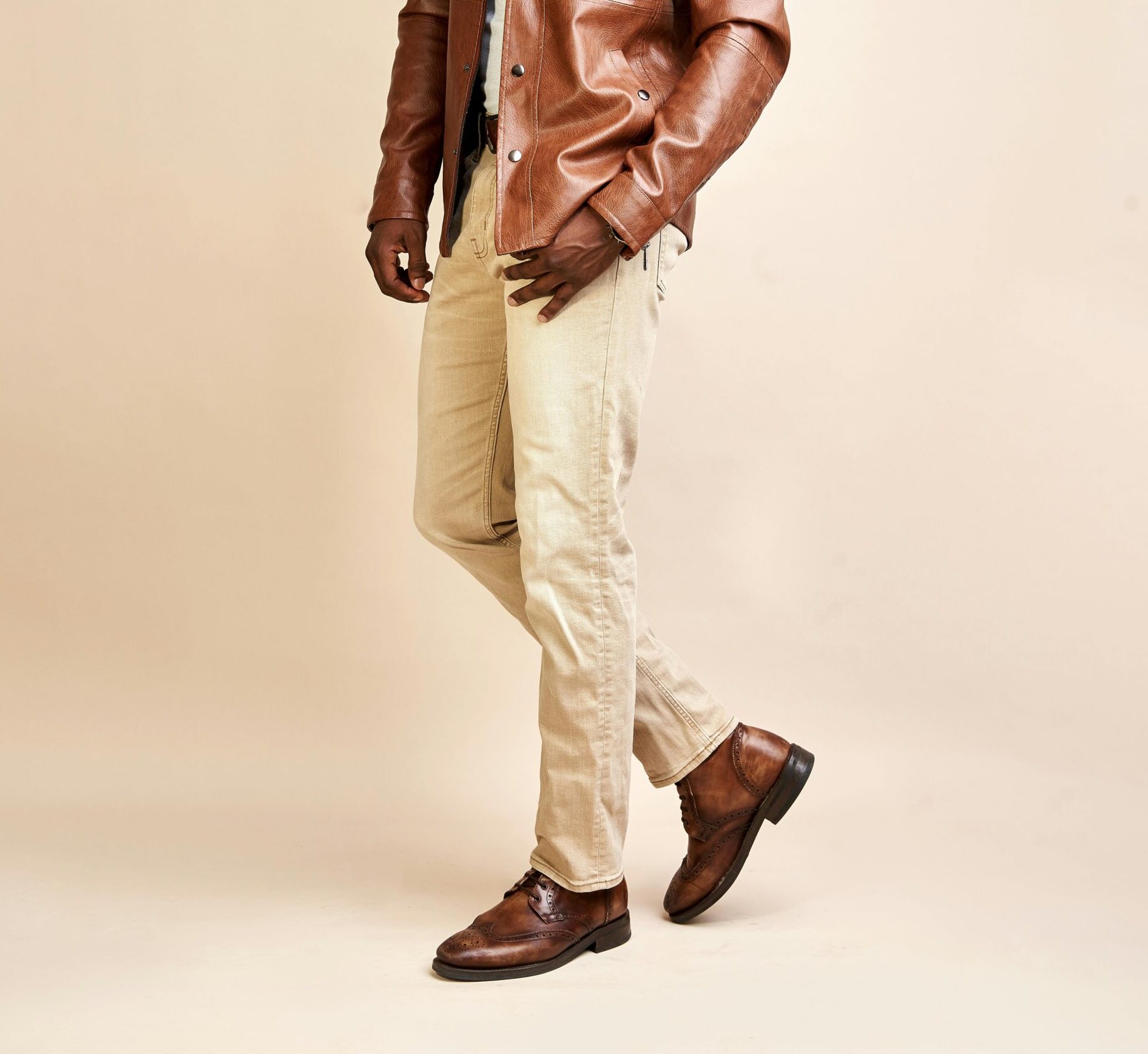 A fashionable man in a leather jacket posing in a studio setting.